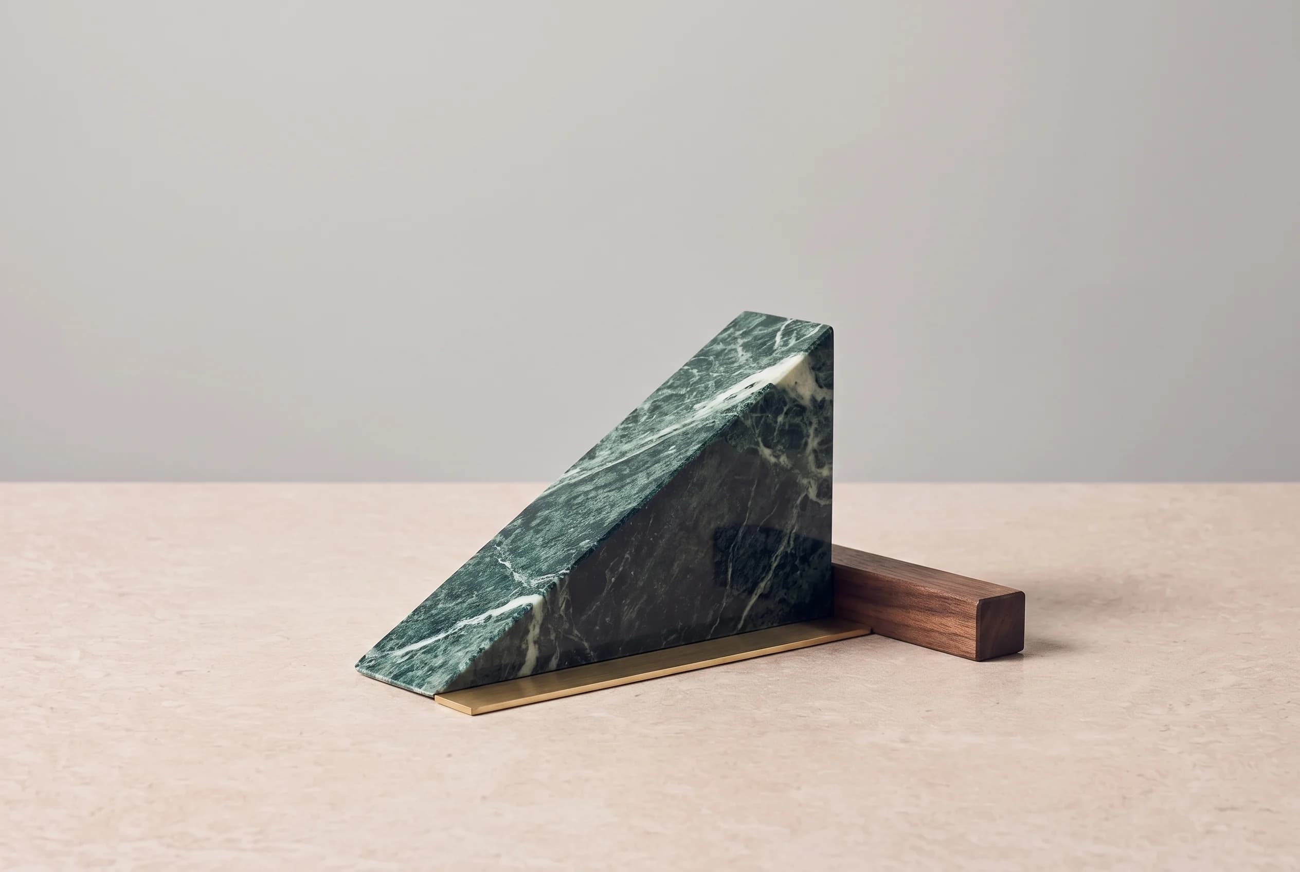 A steep ramp of green marble rises from a stone surface beside a thin brass bar and a dark oak block, lit from the side against a grey wall.
