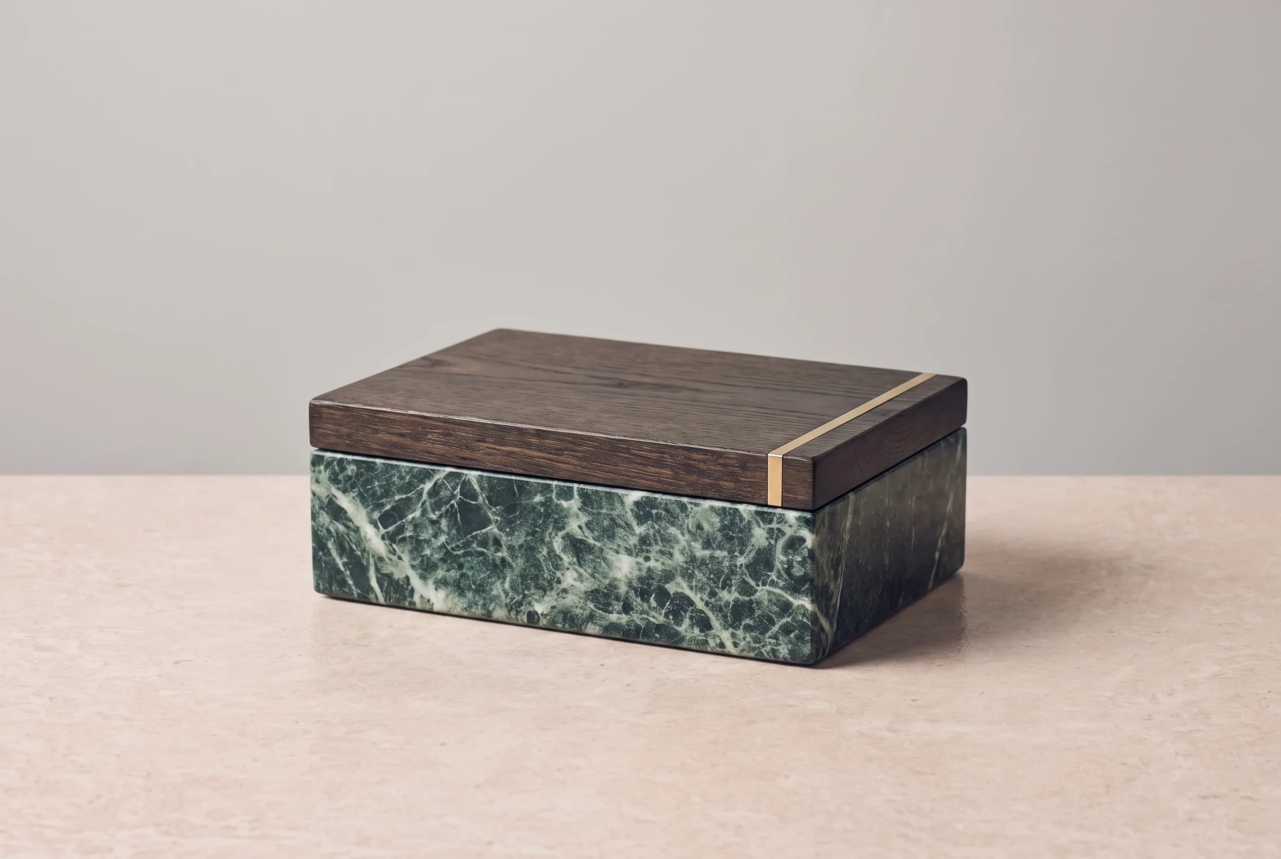A still life of a marble gift box with an oak lid standing on a stone table against a grey wall, lit from the side.